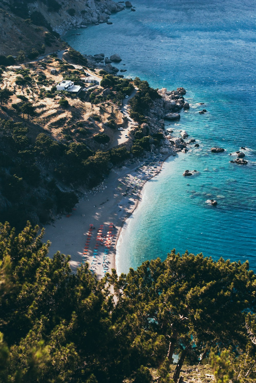 Bovenaanzicht van een wit strand met helderblauw water en rotsen 