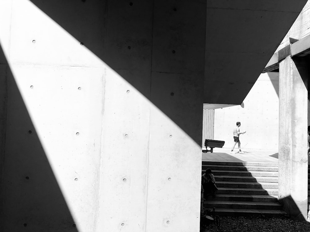 man walking past stairs in sidewalk grayscale photo