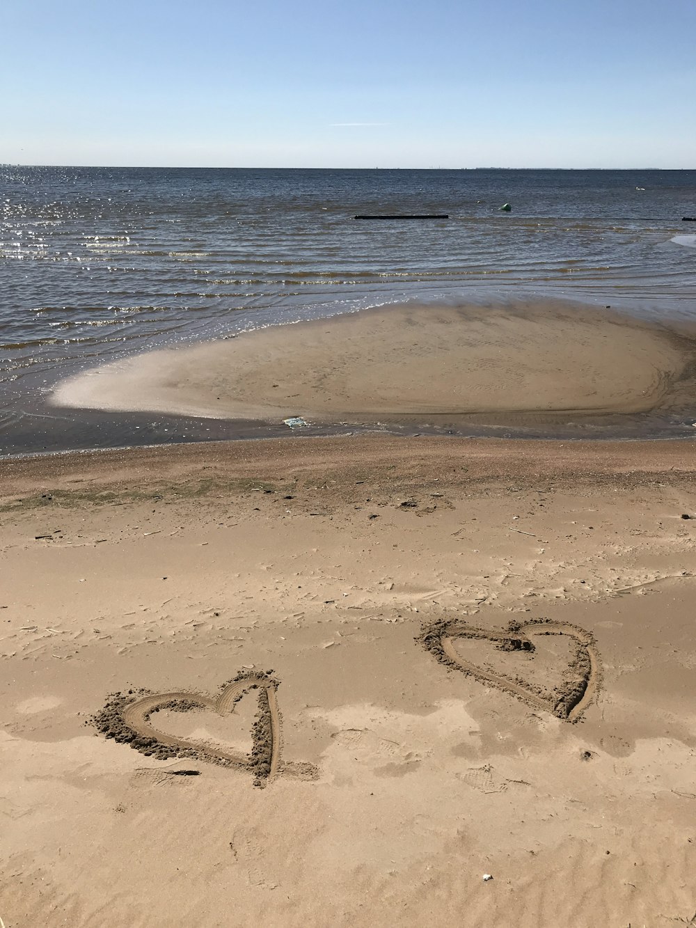 Dois corações desenhados na areia marrom da praia