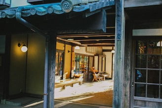 A traditional Japanese interior with wooden architecture, featuring sliding doors and tatami flooring. Soft lighting creates a warm and inviting ambiance, with a few chairs and tables visible in the space.