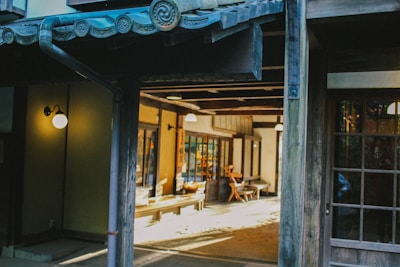 A traditional Japanese interior with wooden architecture, featuring sliding doors and tatami flooring. Soft lighting creates a warm and inviting ambiance, with a few chairs and tables visible in the space.