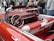 A classic convertible car interior with a vibrant red and white leather upholstery. The steering wheel and dashboard feature a vintage design, perfectly complementing the retro aesthetic of the car. In the background, a group of people stands on a street, partially visible and slightly out of focus.