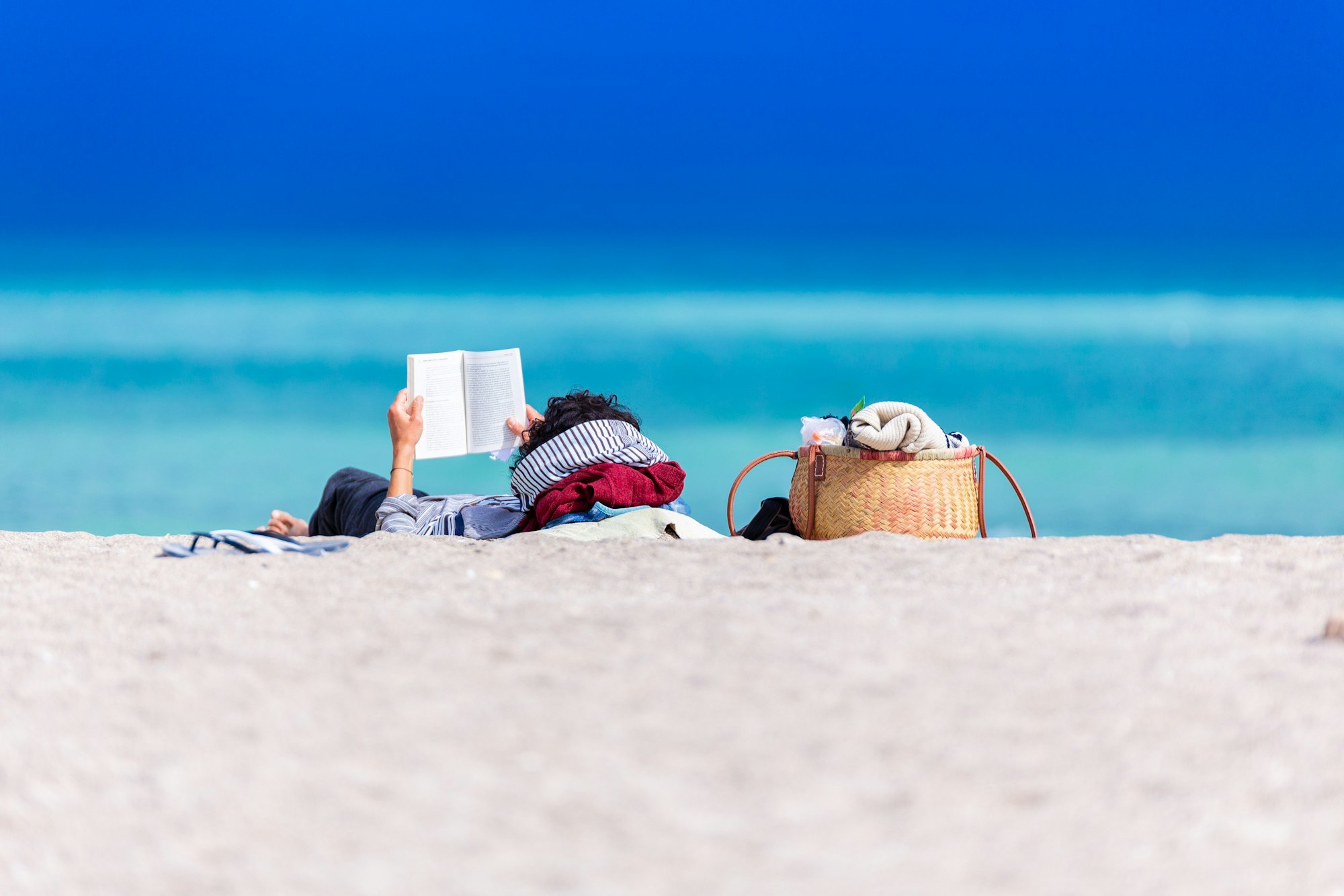 A calm scene featuring a person reading a book on the beach.