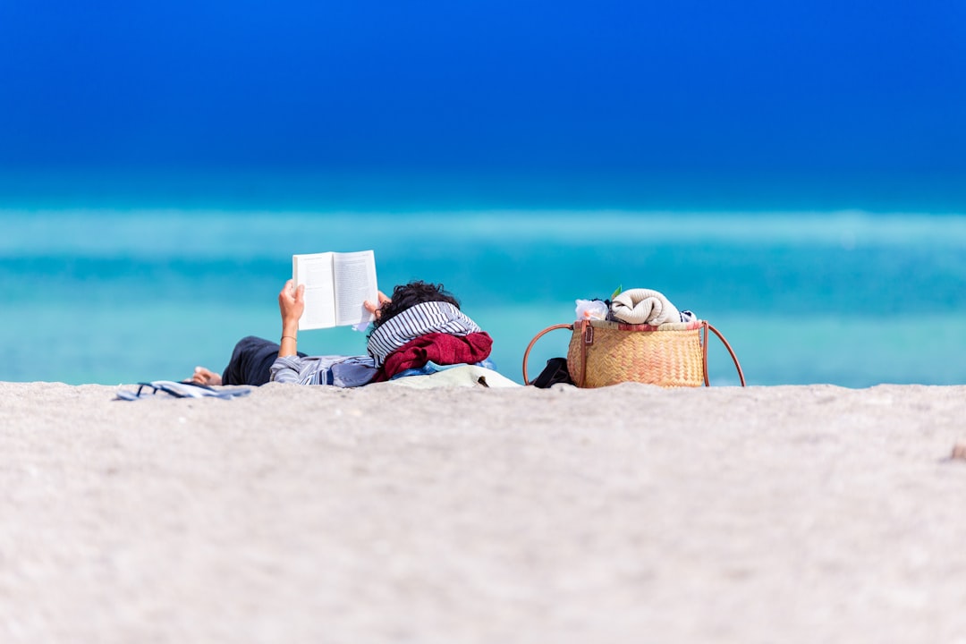 person lying on shore, A calm scene featuring a person reading a book on the beach.