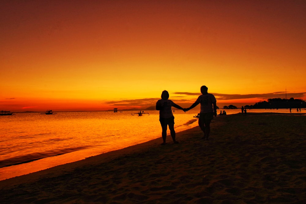 Homem e mulher andando de mãos dadas na praia ao pôr do sol