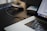 A close-up of a laptop with an open application visible on the screen. A USB cable is plugged into the laptop, with a blurred object that appears to be an external hard drive in the background. The setting is a dimly-lit environment, suggesting a workspace.