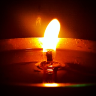 Close-up of a handmade scented candle with a soft glowing flame on a wooden table.