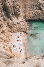 A sunlit, tucked-away beach cove with turquoise water and a few colorful umbrellas.