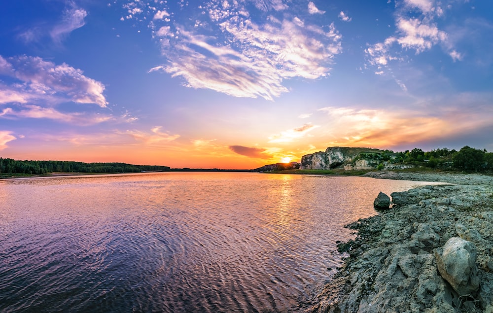 the sun is setting over the water and rocks