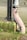 A weathered metal pipe with peeling paint stands next to a vertical black pipe. The pipes are mounted on a concrete block that is partially covered with moss and small patches of grass growing around it, set against a background of paving stones.
