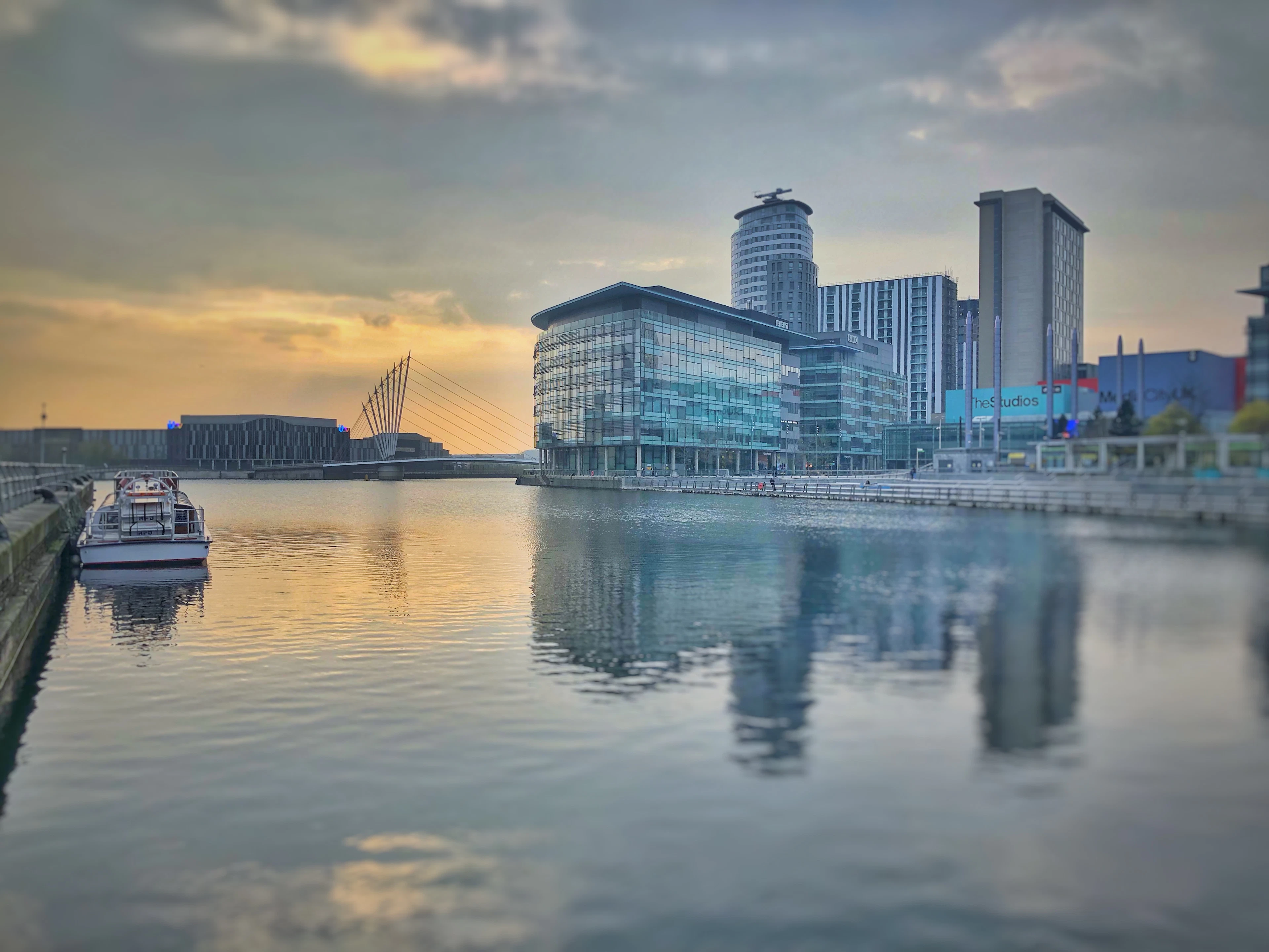 Glass waterfront towers reflected in a calm dock at sunset, with a boat moored alongside