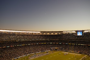 A wide-angle view of a packed stadium with players lined up before kickoff under a clear sky