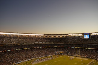A wide-angle view of a packed stadium with players lined up before kickoff under a clear sky