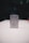 A metallic rectangular lighter sits on a white surface. The lighter is adorned with a geometric emblem, featuring a capital 'G' centered between a compass and square, symbols often associated with Freemasonry. The background is dark and blurred, drawing focus to the foreground object.