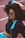 A stylish woman with voluminous curly hair wearing sunglasses and a sporty outfit that includes a black crop top and a jacket with blue accents is seen relaxing on a track field.