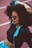 A stylish woman with voluminous curly hair wearing sunglasses and a sporty outfit that includes a black crop top and a jacket with blue accents is seen relaxing on a track field.