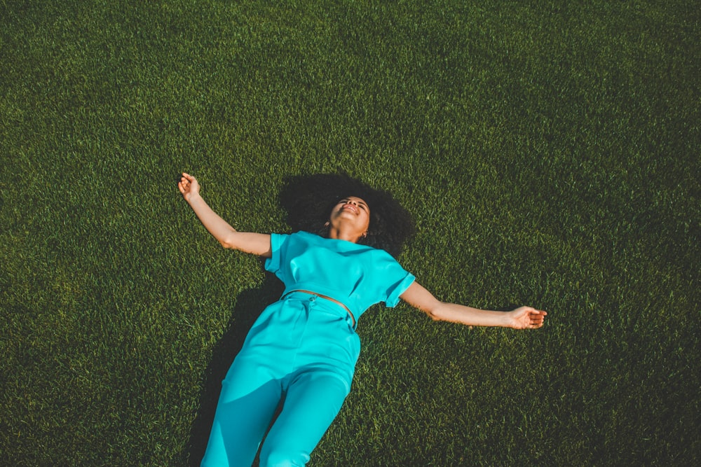 woman wearing blue jumpsuit lying on green grass field