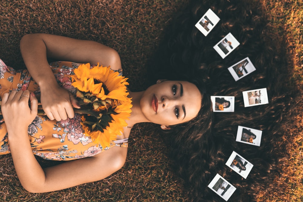 close-up photography of lying on woman on brown grass while holding sunflower
