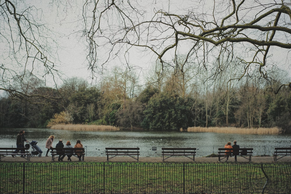 unknown persons sitting on brown bench near body of water