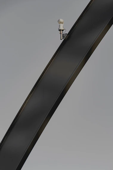 A sleek security camera mounted on a steel beam overlooking an active construction site at dawn.