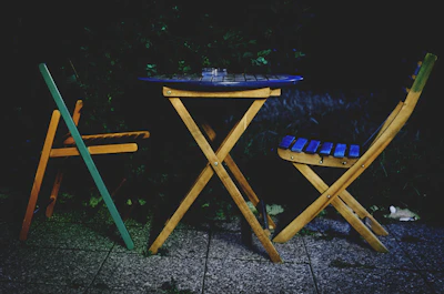 Outdoor scene showing a minimalist metal table with chairs arranged for an evening gathering.