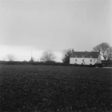 An old black-and-white photograph of the Mathias family farmhouse surrounded by tall trees and a picket fence.