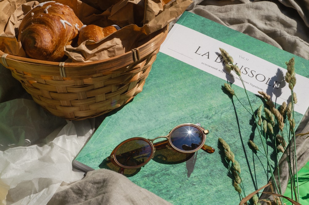 cesta llena de pan, libro verde y blanco y gafas de sol
