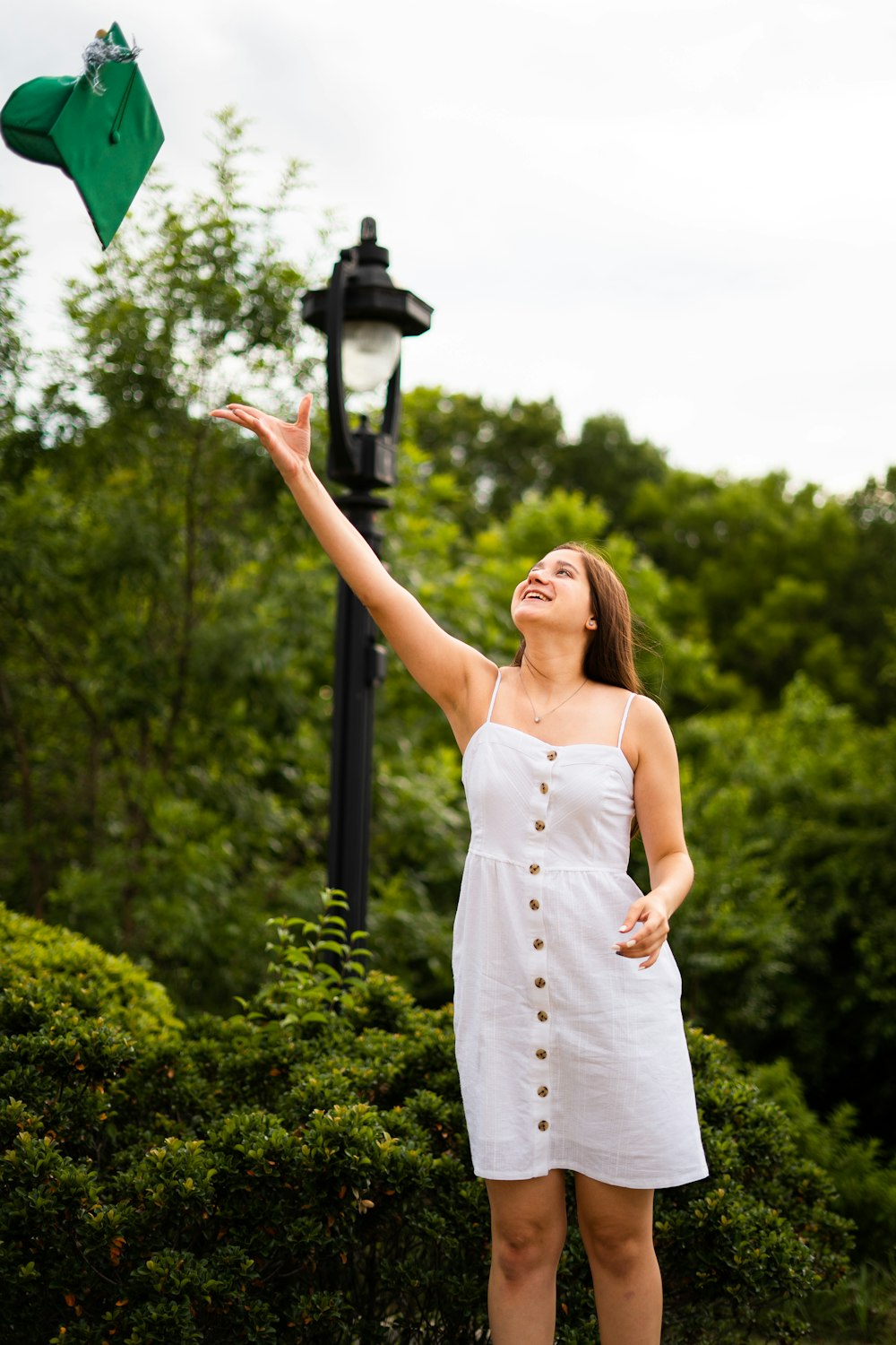 woman wearing white dress throwing green academic hat