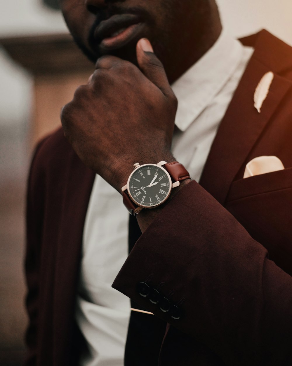 man wearing round silver-colored analog watch and brown suit jacket