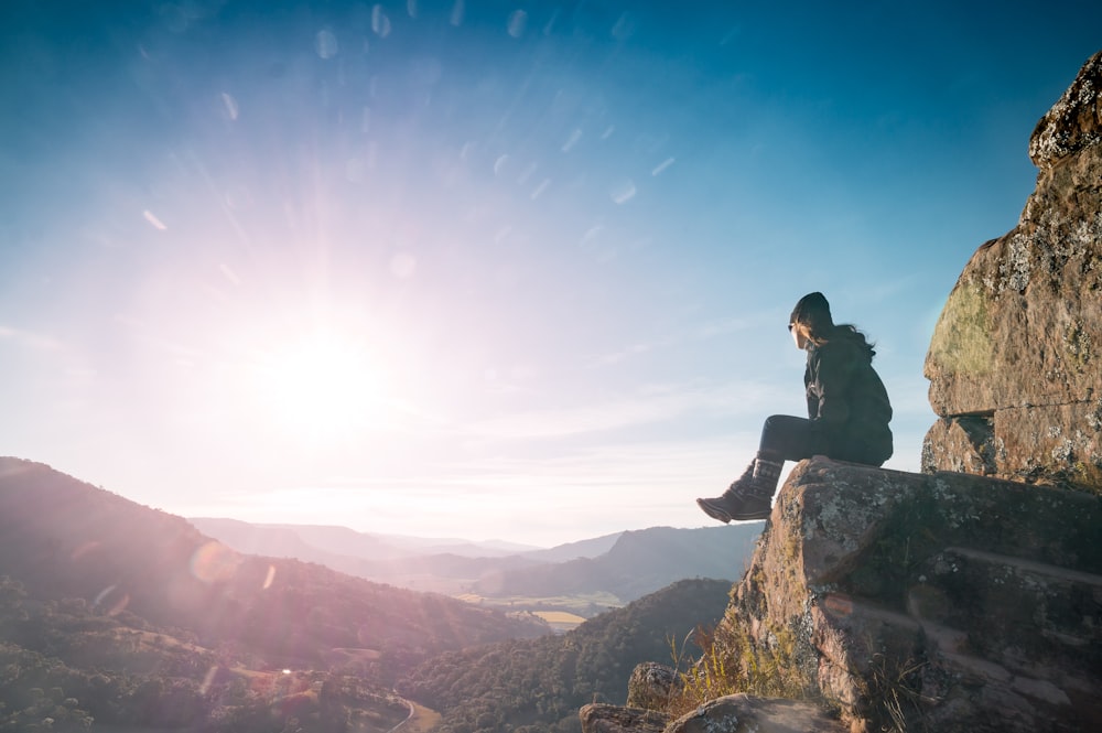 man wearing jacket sitting on grey rock