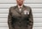 A person is wearing a military uniform with several medals attached to the chest. The background consists of light-colored horizontal panels.