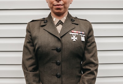 A person is wearing a military uniform with several medals attached to the chest. The background consists of light-colored horizontal panels.