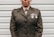 A person is wearing a military uniform with several medals attached to the chest. The background consists of light-colored horizontal panels.