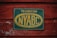 A weathered sign attached to a rustic, red-painted wooden surface. The sign is rectangular with a dark green background and a faded yellow oval around the letters 'NYABC'. It contains text that reads 'Technician New York Artificial Breeders' Cooperative, Inc.' The wooden texture shows signs of peeling paint and age.