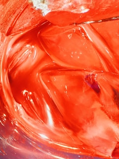 Bright red liquid with visible ice cubes creating a refreshing and energetic appearance. The light reflection on the ice adds a glossy texture to the image.
