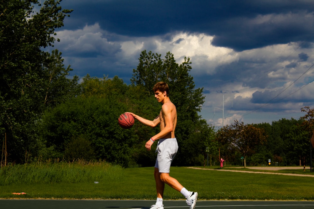 topless man holding basketball during daytime