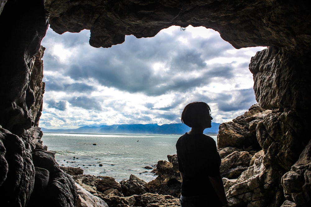 person standing on rock formation cave during daytime