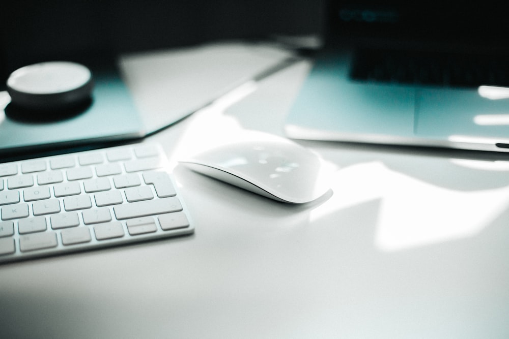 Apple Magic mouse beside keyboard on white surface