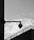 A surveillance camera is mounted on a wall with a stark, industrial design. The background consists of a cloudy sky and a large building edge, giving off a minimalist, urban feel.