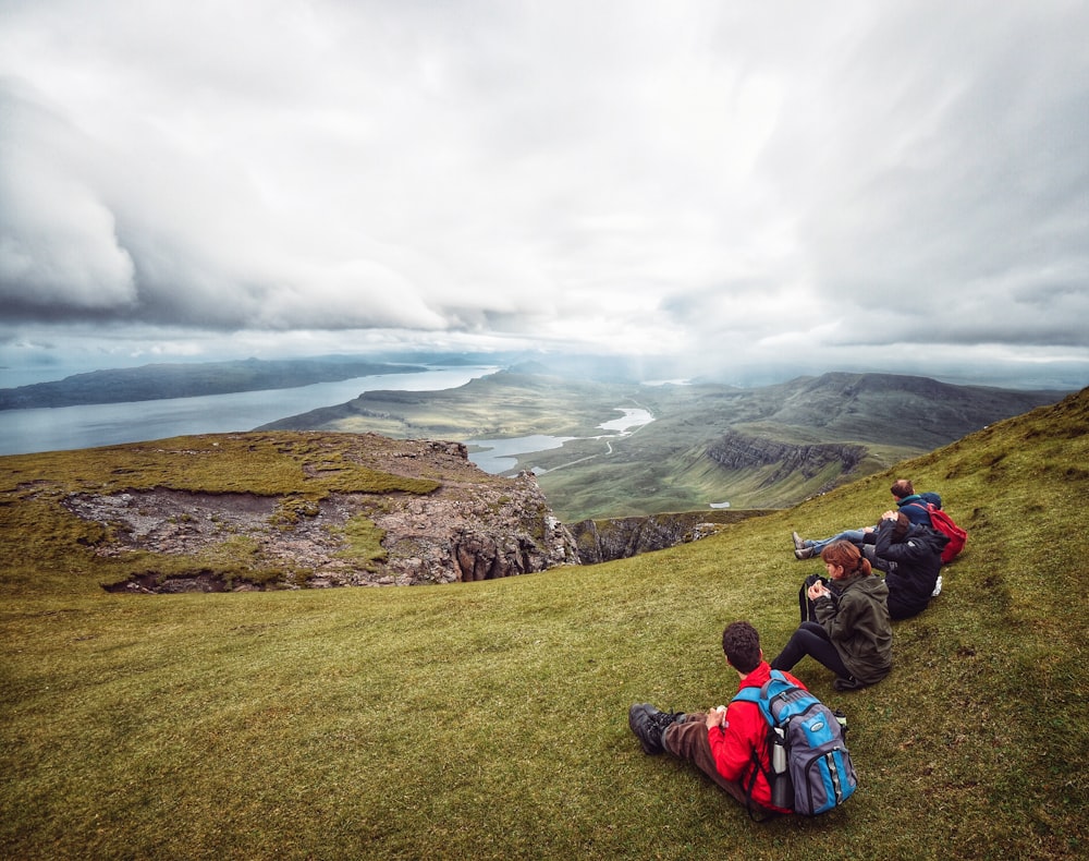 three person sitting on green mountain