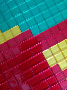 A grid pattern made of square tiles in bright, glossy shades of teal, yellow, and red.