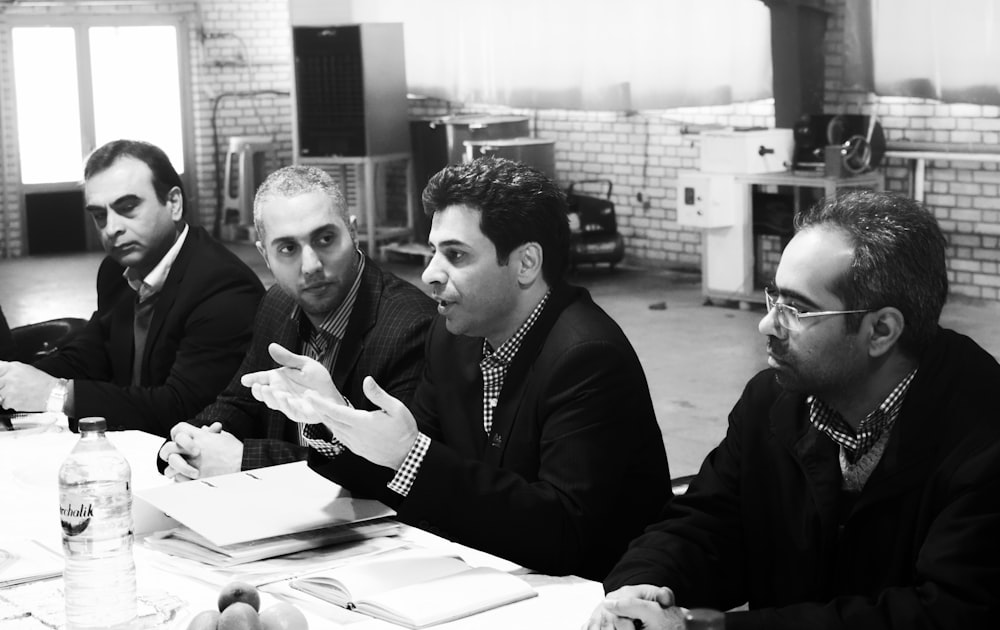 four men sitting at the table grayscale photo