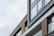 A modern building facade with large glass windows and stylish horizontal wooden slats. The architecture features clean lines and a minimalist design, highlighted by a combination of gray and neutral tones.