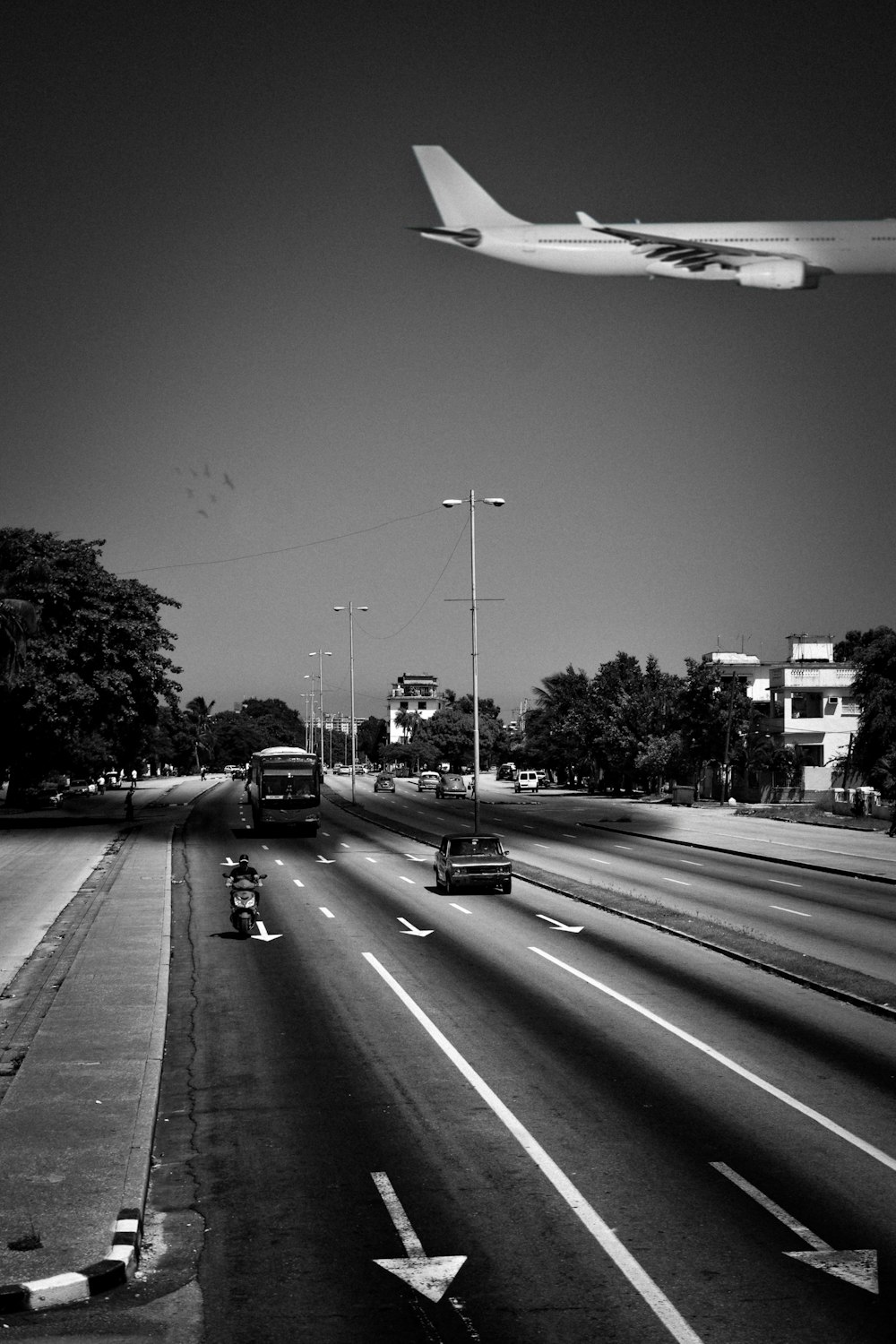 grayscale photo of passenger plane passing highway with vehicles