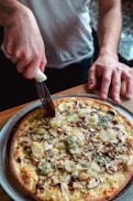 person standing and about to slice pizza