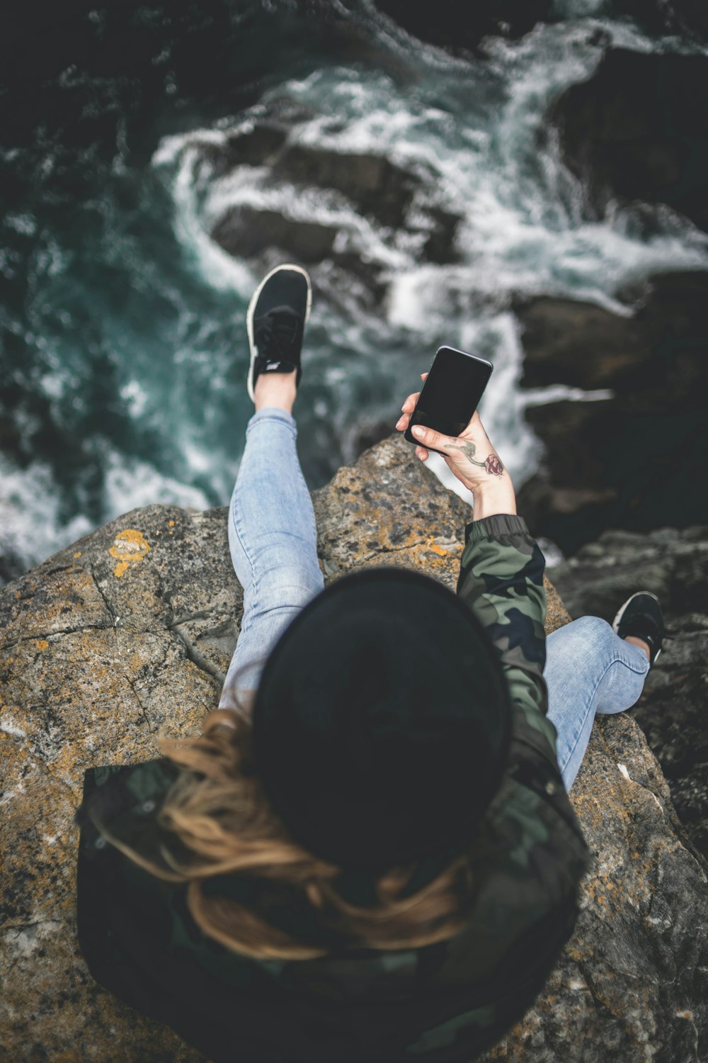 woman holding smartphone while sitting on cliff