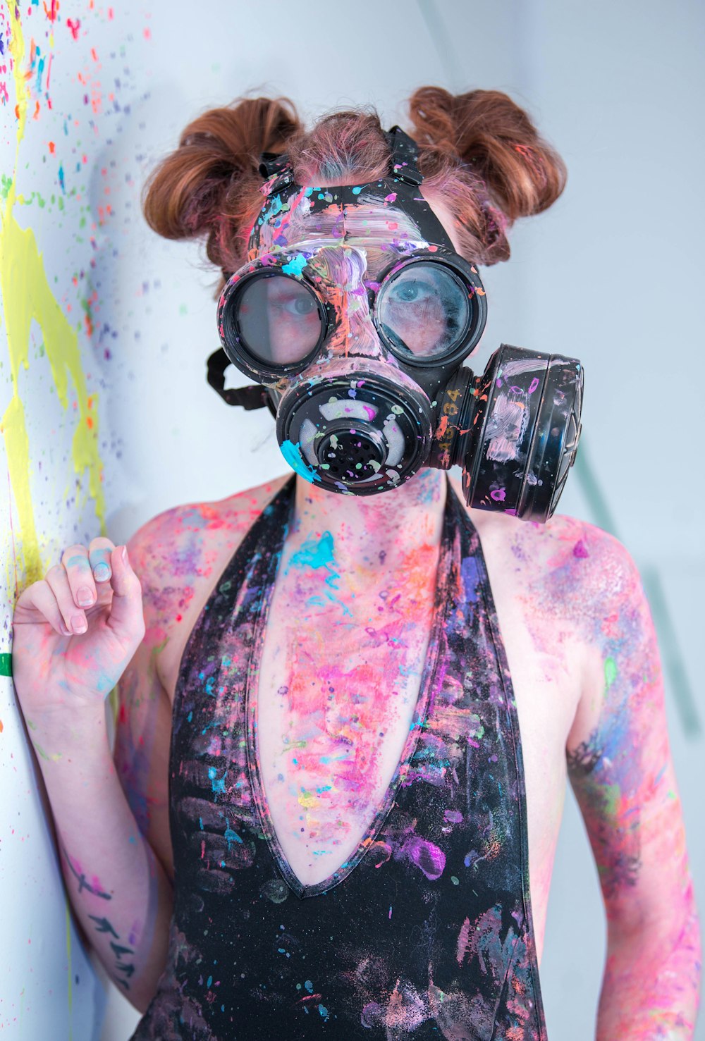 multicolored paint splattered woman wearing black monokini and gas mask standing beside wall