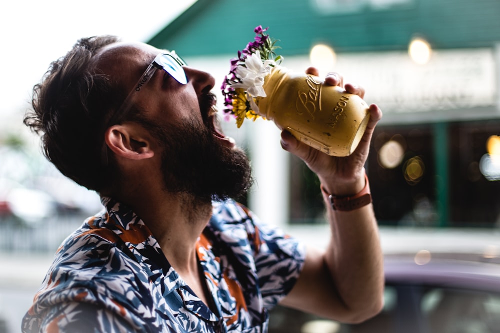 man holding flowers in mason jar towards mouth