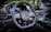 A luxury car interior featuring a sleek design with a focus on the steering wheel. The dashboard includes modern digital displays and metallic accents, enhancing the overall elegance and sophistication. The ambient lighting and polished surfaces reflect a high level of craftsmanship.