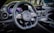 A luxury car interior featuring a sleek design with a focus on the steering wheel. The dashboard includes modern digital displays and metallic accents, enhancing the overall elegance and sophistication. The ambient lighting and polished surfaces reflect a high level of craftsmanship.